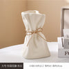 A beige ceramic money bag shaped vase with a twine bow on a white surface.