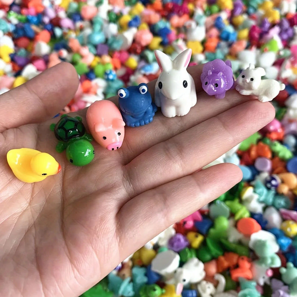 A hand holds various colorful resin miniature figurines including a white rabbit, blue frog, pink, and green animals.