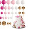 A set of twenty pink and white ball cake toppers on sticks arranged around a white tiered cake.