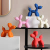 A collection of pink and blue balloon dog resin sculptures displayed on a black shelf against a neutral wall.