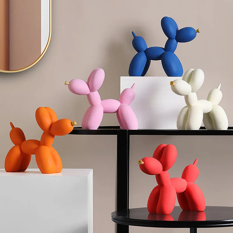 A collection of pink and blue balloon dog resin sculptures displayed on a black shelf against a neutral wall.
