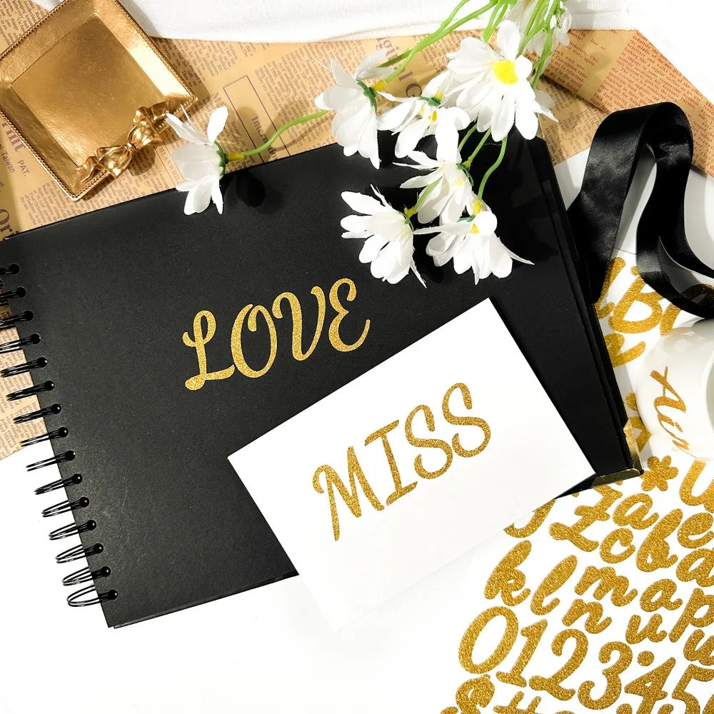 A black notebook with gold lettering and white paper, decorated with white flowers and a black ribbon.