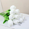 Un ramo de tulipanes de PU blancos artificiales con hojas verdes, exhibido sobre una superficie blanca.