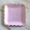 A square pink party plate with a gold rim and scalloped edge.
