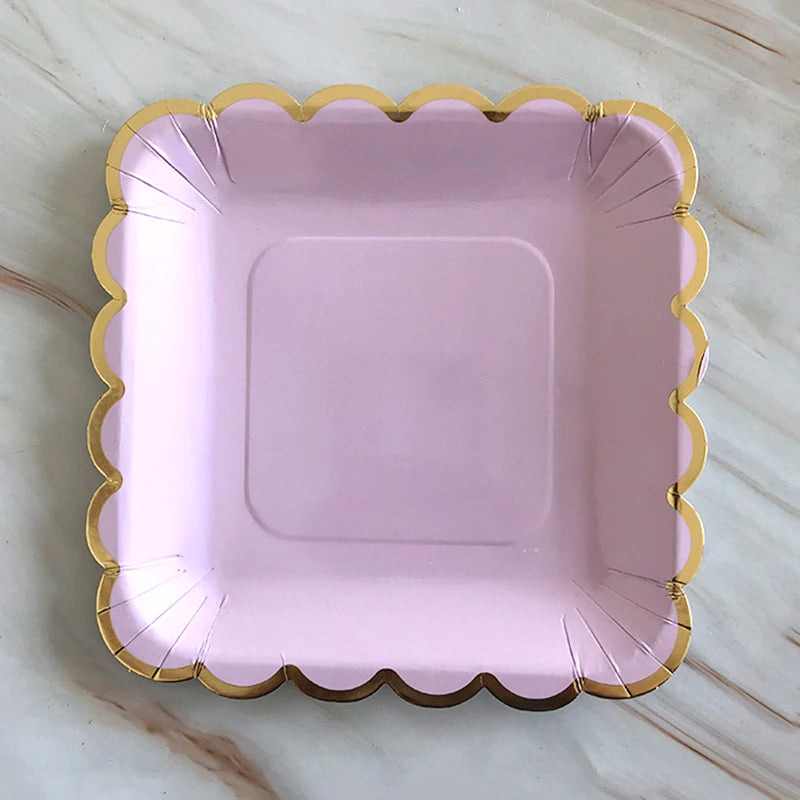 A square pink party plate with a gold rim and scalloped edge.