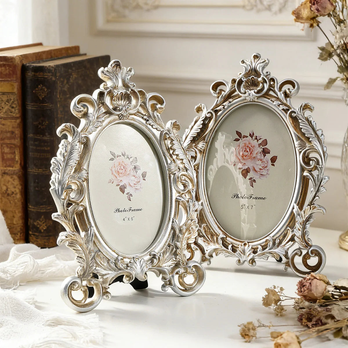 A vintage gold oval resin picture frame displayed on a white surface next to stacked books and dried flowers.