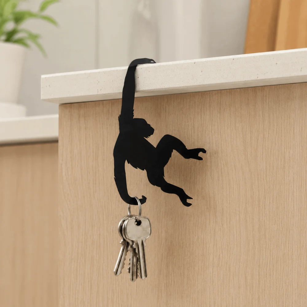 Black monkey-shaped storage hook with a banana design mounted on a light wood cabinet.