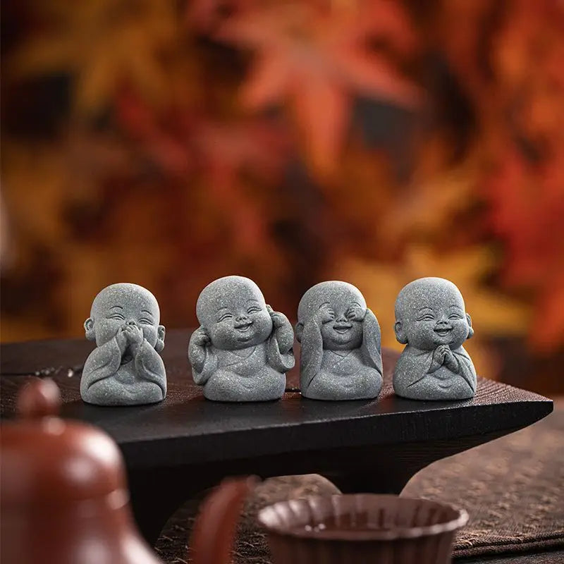A set of small, gray stone monk statues for meditation and Zen decor placed on a dark wooden surface.