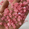 Una mano sostiene una pila de aderezos de uñas acrílicos en forma de corazón rosa.