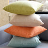 A set of two solid color linen pillows, one olive green and one peach, resting on a gray sofa.
