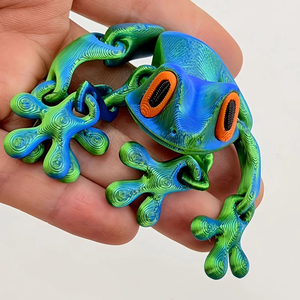A realistic, movable 3D printed frog fridge magnet in vibrant green and blue colors held in a hand.