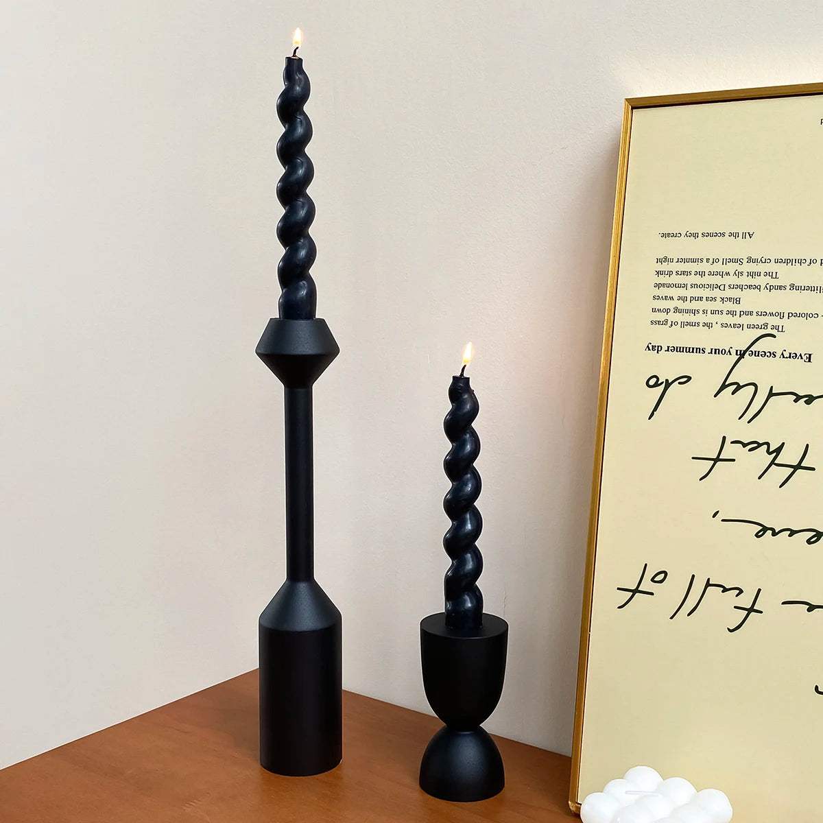 A set of two black, fluted candle holders with lit candles displayed on a wooden surface.