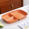 An orange 3-compartment portion control plate is shown on a white surface next to a lime and a book.