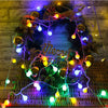 A festive wreath decorated with battery-powered globe string lights and greenery.