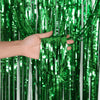 A hand is holding a strand of metallic green foil fringe curtain hanging vertically.