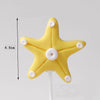 Yellow starfish cake topper with five small white dots on a white stick.