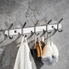A set of six polished stainless steel wall-mounted hooks hanging against a gray concrete background.