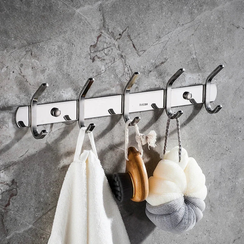 A set of six polished stainless steel wall-mounted hooks hanging against a gray concrete background.