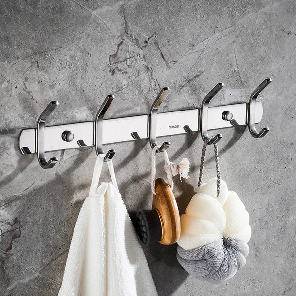 A set of six polished stainless steel wall-mounted hooks hanging against a gray concrete background.