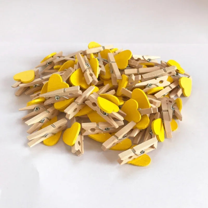 A pile of small, heart-shaped wooden photo clips in yellow and natural wood tones.