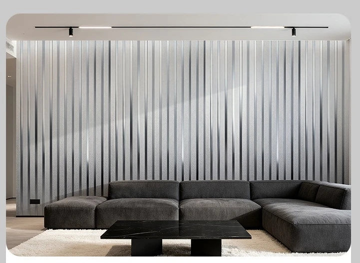 A modern living room featuring a dark gray sectional sofa and coffee table in front of a vertical metallic gold striped wall 