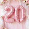 Pink foil number balloons spelling '20' decorated with pink floral garlands and sheer fabric backdrop