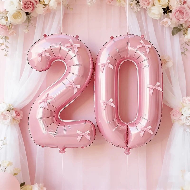 Pink foil number balloons spelling '20' decorated with pink floral garlands and sheer fabric backdrop