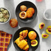 A dark plate holds golden pastries and fruit slices on a light gray surface.