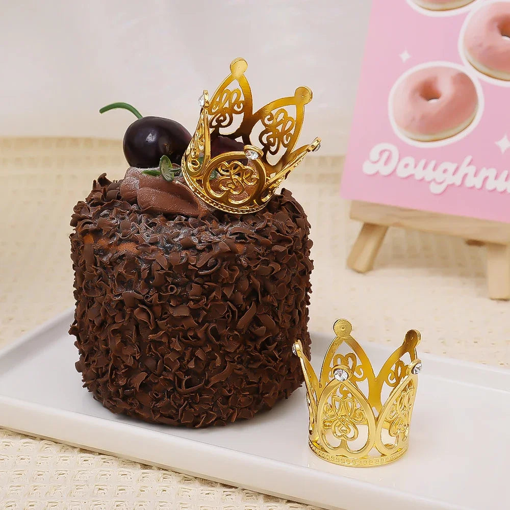A dark chocolate cake decorated with a gold crown topper and surrounded by chocolate shavings.