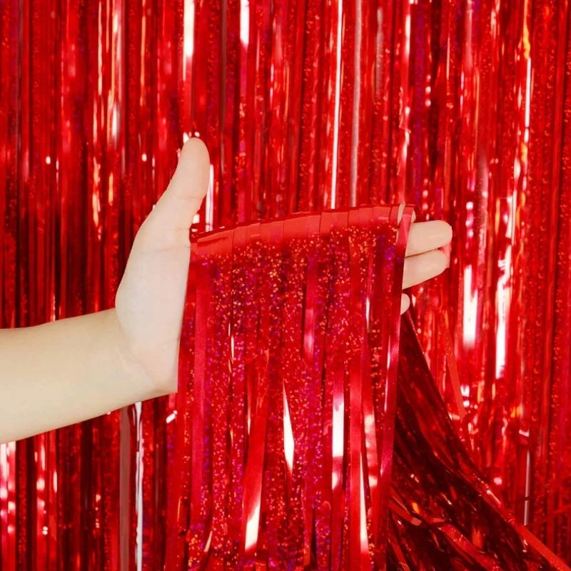 A hand holds a shimmering red metallic foil tinsel fringe backdrop set against a vibrant red curtain.