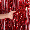 A hand reaches through a curtain of red and white metallic foil fringe.