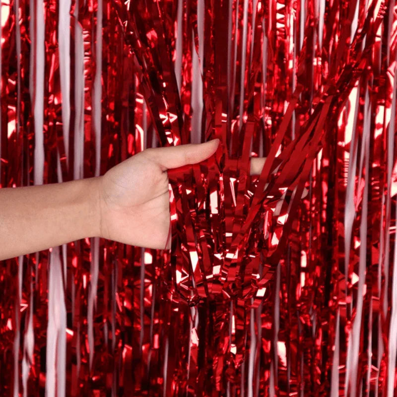 A hand reaches through a curtain of red and white metallic foil fringe.