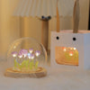 A clear glass dome holds glowing purple and green LED tulips inside a white wooden night light holder.