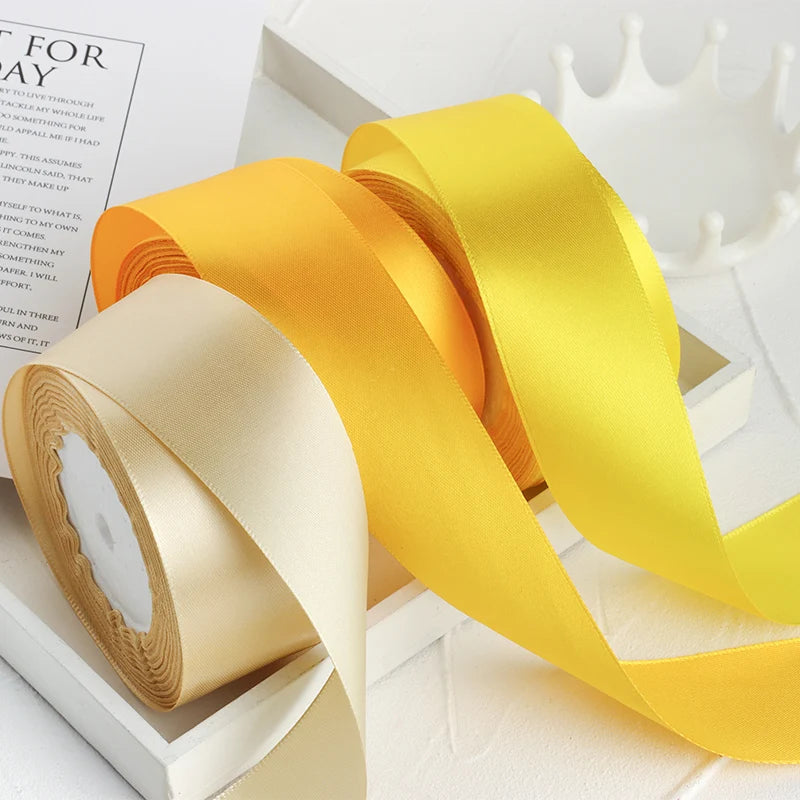 Un ensemble de rubans décoratifs en satin or et jaune, présentés sur une surface blanche.