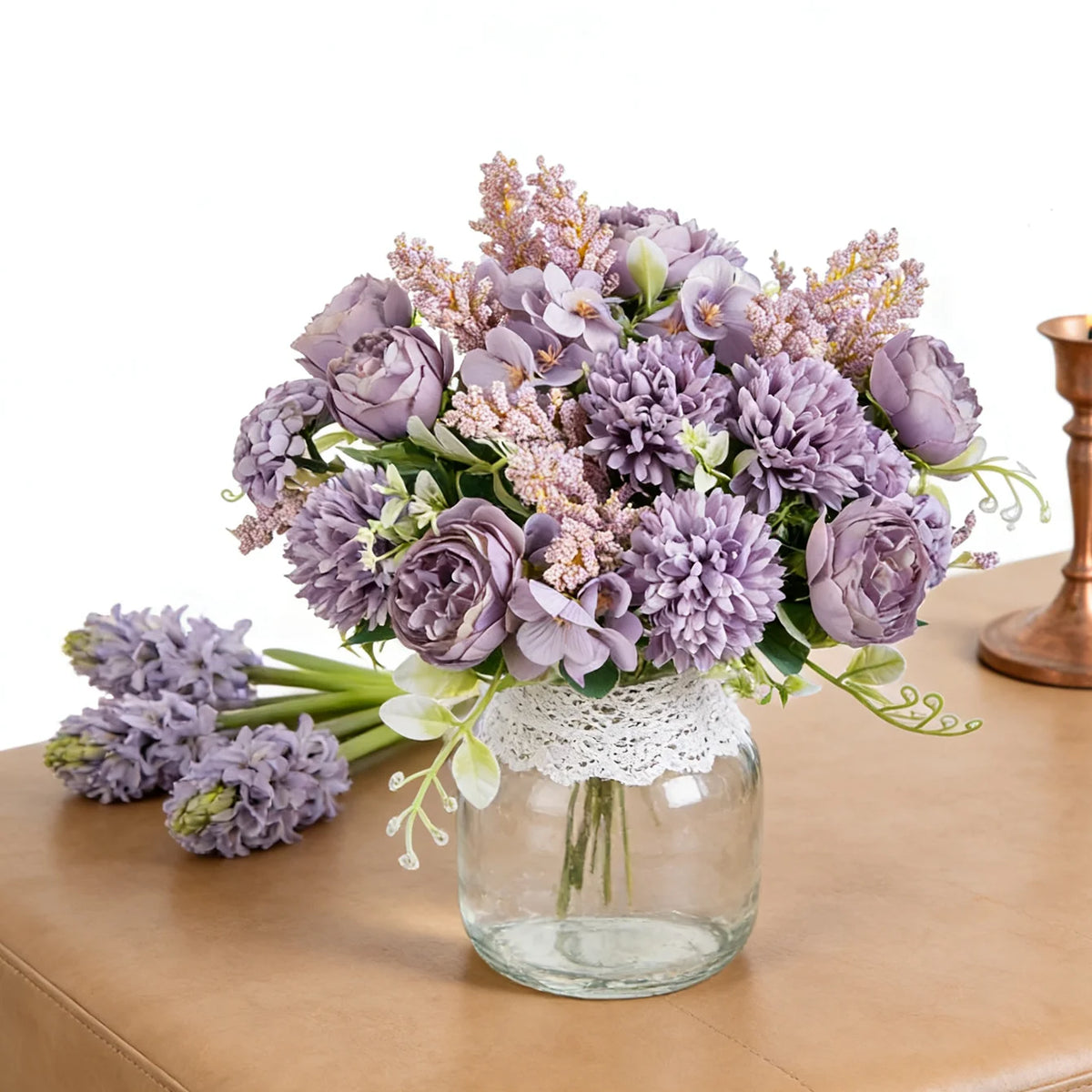 A bouquet of artificial silk peony flowers in shades of purple and lavender arranged in a clear glass vase.