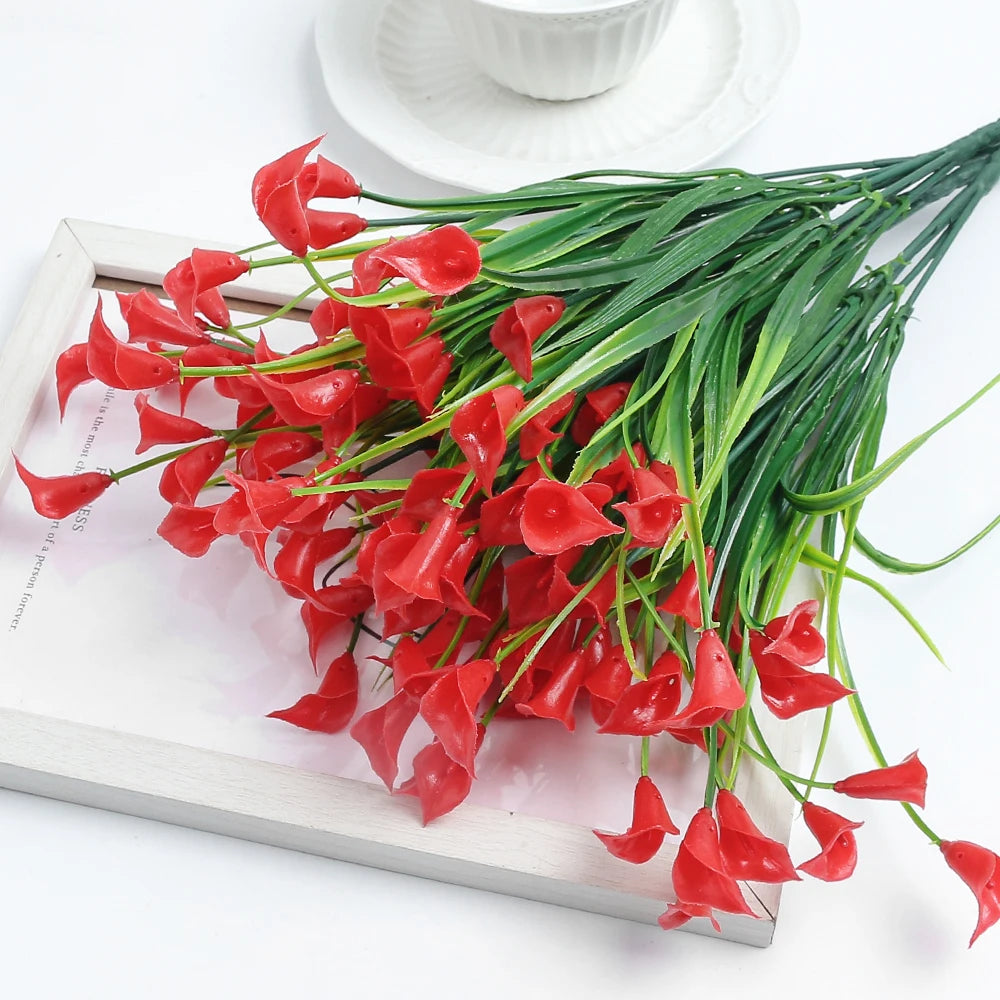 A bouquet of bright red artificial calla lily silk flowers with green stems displayed on a wooden tray.