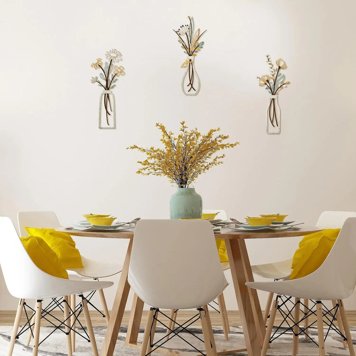 Three glass vases with dried flowers are displayed on a white wall above a wooden table.