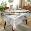A white and gold marble-printed tablecloth draped over a wooden table in a bright room.