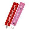 A red woven tag and a pink woven tag for the Kiss Me Before Flight keychain.