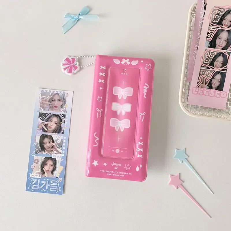Un álbum de cabina de fotos rosa con elementos decorativos y una cinta azul claro, junto a un pequeño accesorio rosa.