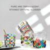 A collection of pure and translucent stained crystal whiskey glasses with various facets and colors.
