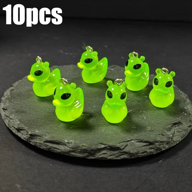 Ten glow-in-the-dark green cartoon alien kitty duck resin charms displayed on a dark surface.