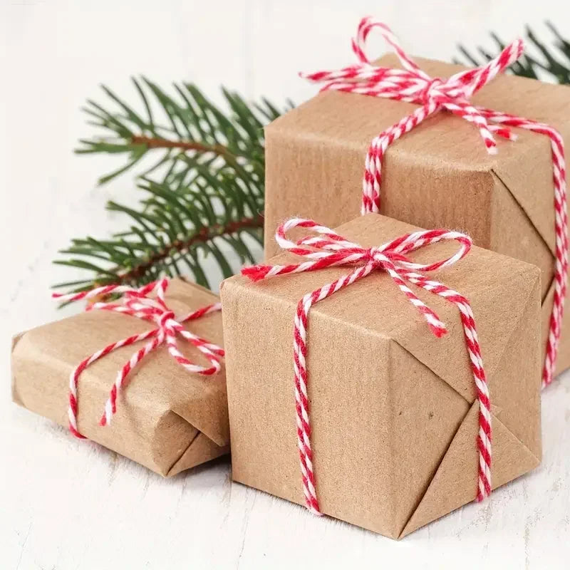 Brown gift boxes tied with red and white striped cotton twine resting on a white wooden surface.