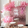 A pink and white sequin wall backdrop decorated with clusters of pink and white balloons and a pink bow for a birthday party.