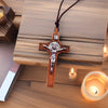A wooden cross necklace with a wax rope cord resting on a wooden surface next to a lit candle.