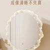 A round vanity mirror with a ruffled white frame and illuminated glass, displayed on a stand.