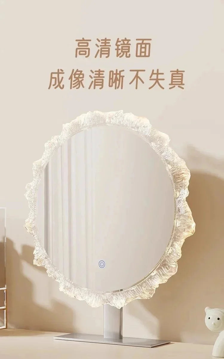 A round vanity mirror with a ruffled white frame and illuminated glass, displayed on a stand.