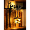 A vintage gothic bookshelf reading lamp with an ornate wrought iron bracket and warm amber glow illuminating stacked books.
