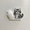 A small, gray and black cat face decoration made of acrylic is mounted on a white magnetic strip.
