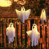 A row of white LED ghost hanging decorations are displayed on a wooden fence at sunset.